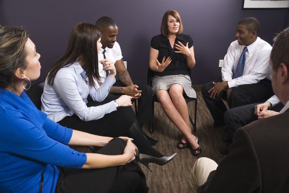 A photo of people sitting around in a circle like a support group.