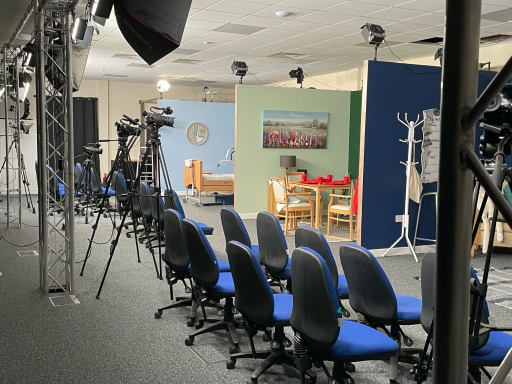 A photo showing the length of the film studio with the sets on one side and the chairs on the other, underneath the lighting gantry