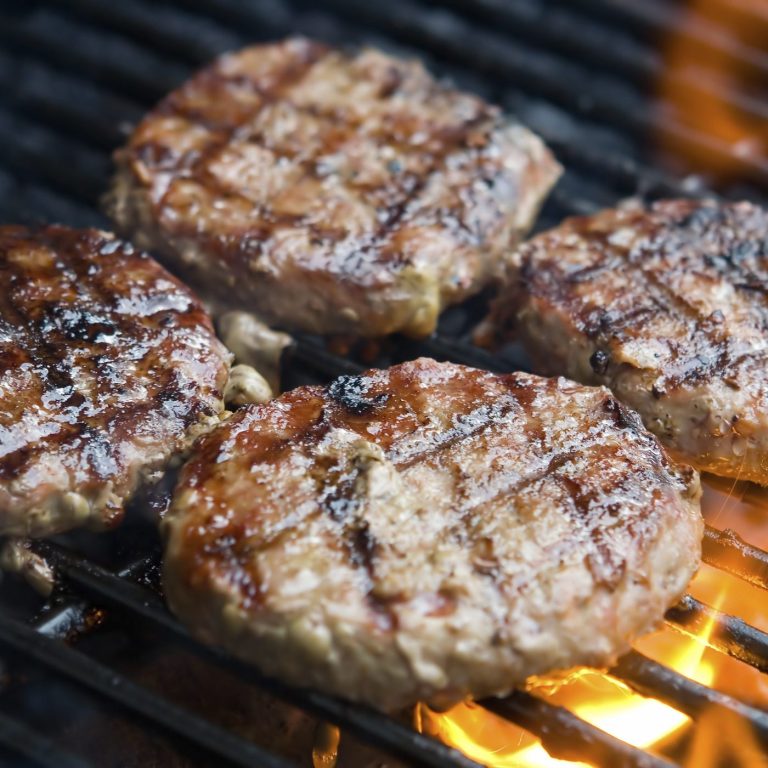 A photo of 4 juice burgers on a grill with grill marks.