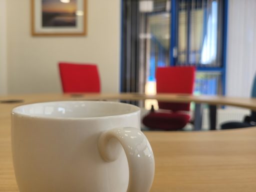 A close up of a big coffee mug on the boardroom table with a blurred background of the chairs opposite.