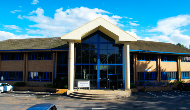 A photo of the outside of the venue with a large porch with steps to the door, a ramp to the right, and blue sky in the background