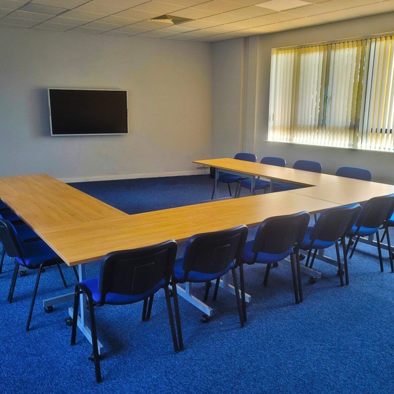 Photo of an empty training room with a u-shape layout of the tables and chairs focused on a large screen on the wall