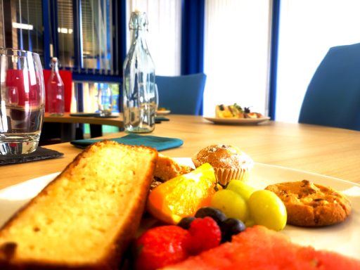 A close up photo of a plate of cakes and fruit on a boardroom table.