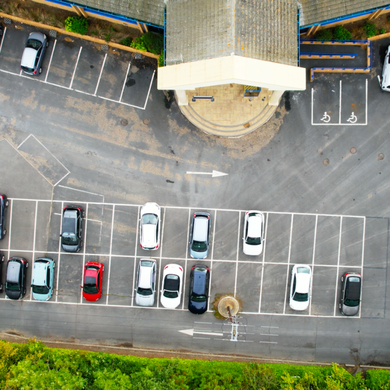 An aerial photo of a carp park with several spaces filled with cars and other empty spaces.