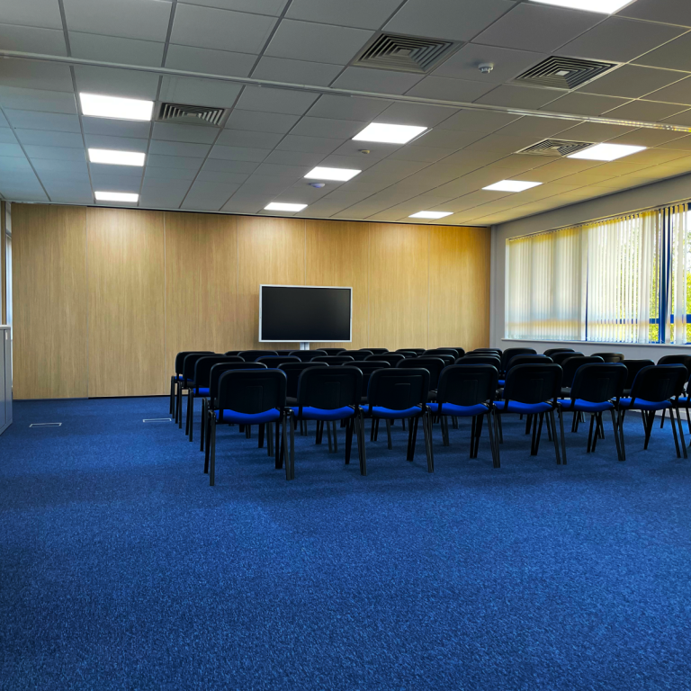 A small photo of a boardroom meeting room with circular table and colourful cushioned chairs.