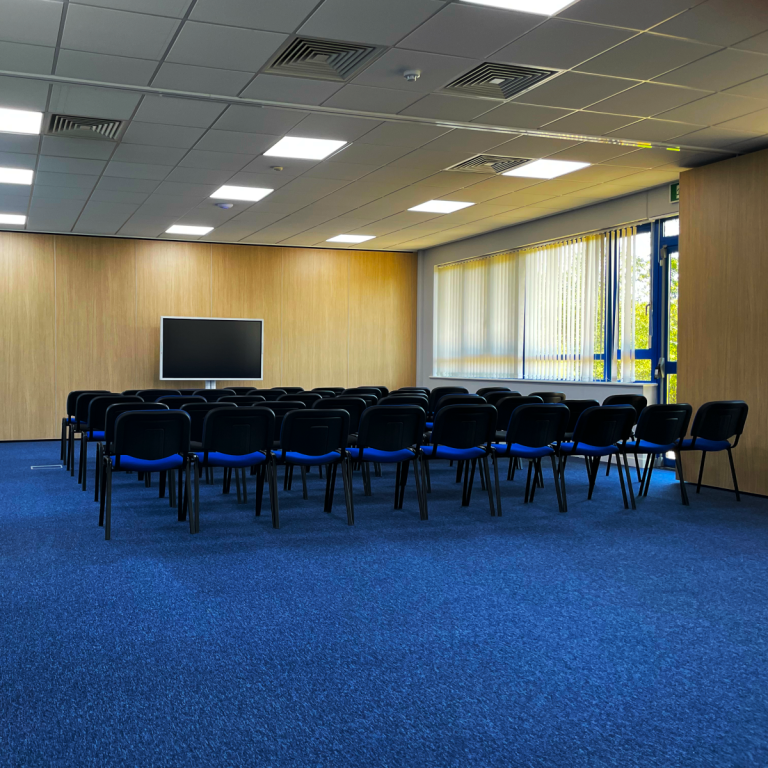 A photo of a large training room with a theatre layout focused on a large smart screen