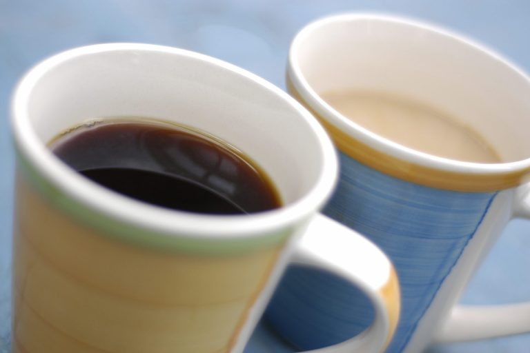 A close up photo of two cups, one with black coffee in and the other with tea in it.