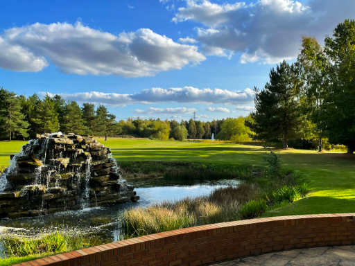 A view of a hole on the golf course taken from behind the water fountain with trees lining the view.