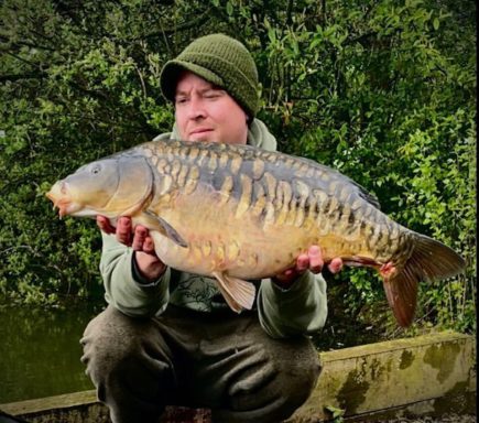 A fisherman holding a large mirror carp.