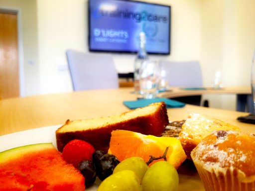 A close up of a plate on the boardroom table with cake and fruit.