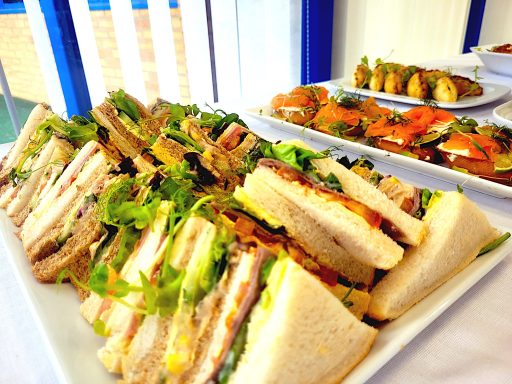 A close up photo of a large platter of nicely filled sandwiches with other buffet dishes in the background.