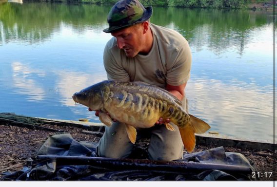 A photo of an angler wearing a hat and holding up a mirror carp