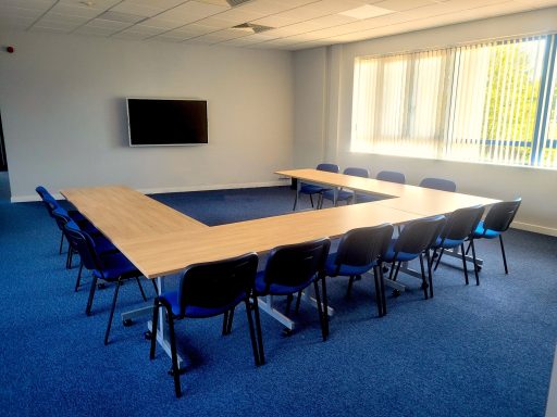 A wide photo of an empty meeting room with a u-shape layout of the tables and chairs.