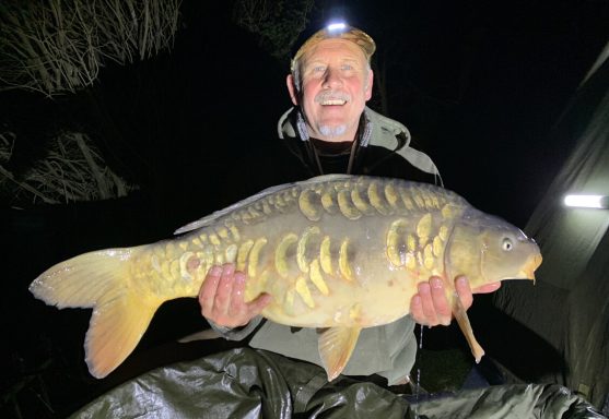 A photo of a fisherman smiling and holding up a mirror carp