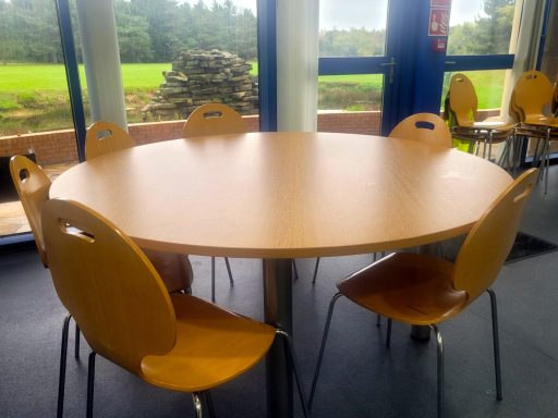 A large circular lunch table with matching chairs around it and a golf course view through the large windows