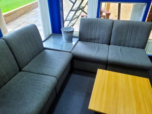 A photo of a seating area in a staffroom with cushioned grey sofas and a wooden square coffee table.