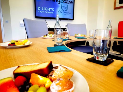 A photo of the boardroom for hire with nice plates of food around. In the foreground is a plate of cakes and fruit.