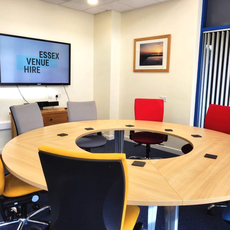 A small photo of a boardroom meeting room with circular table and colourful cushioned chairs.