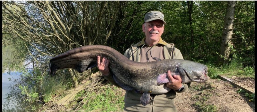 A photo of a smiling fisherman holding up a catfish