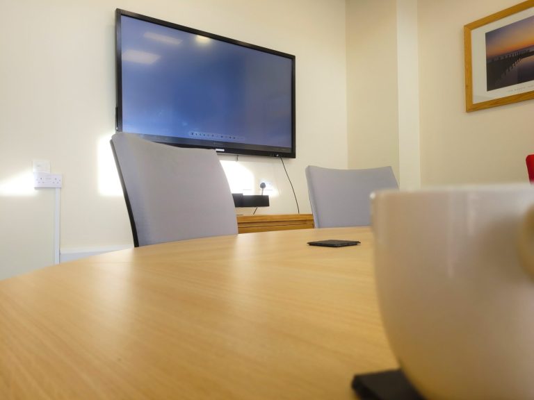 A close up of a large coffee mug on the round boardroom table with the TV in the background