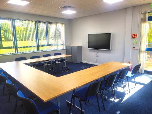 A photo of a u-shape layout training room. A 65" smart screen TV on the wall and a view out the window of a golf course