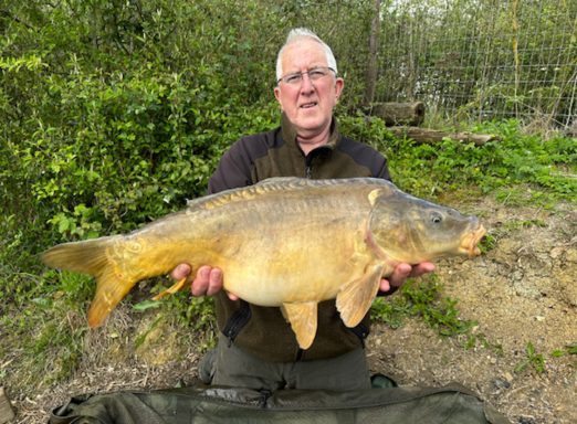 A fisherman holding a large mirror carp.