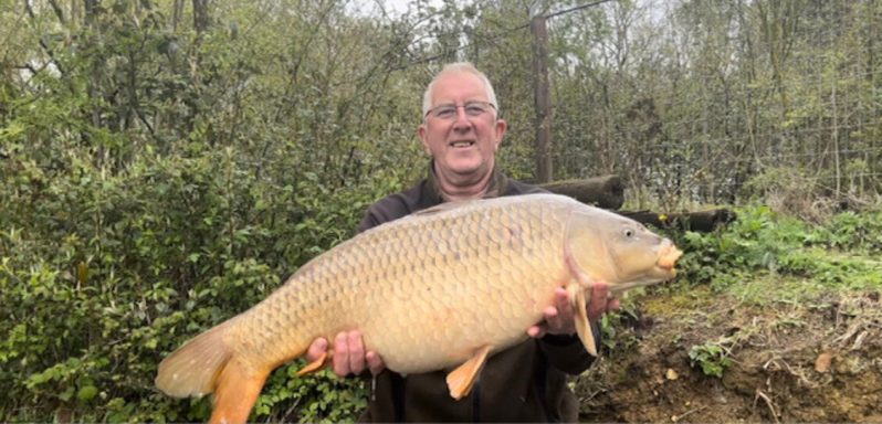 A photo of a fisherman smiling holding a large common carp.