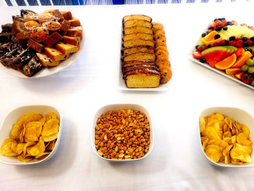 A photo of part of a buffet table with cakes, fresh fruit, and bowls of crisps and nuts.