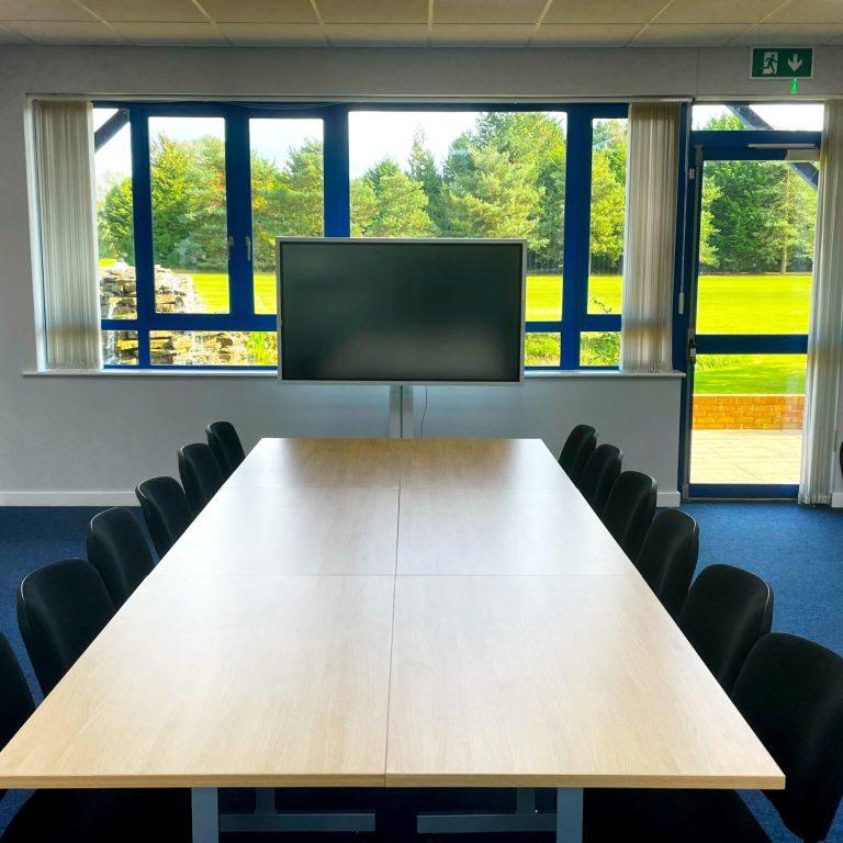 A small photo of a boardroom style meeting room with a 65" smart screen at the head of the table.