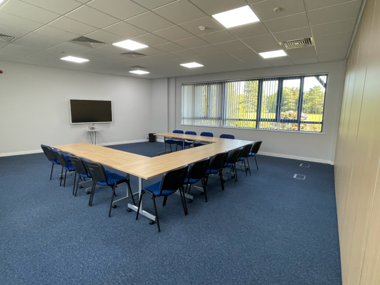 An empty training room with a u-shape layout of tables and chairs, for 10-people, with a focal point of a 65" smart screen on the wall.