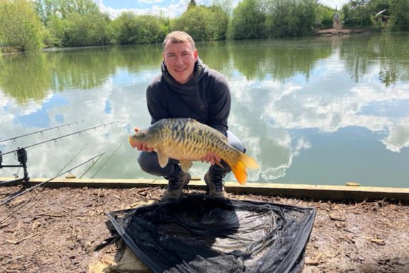 A photo of an angler on the bank holding a mirror carp.