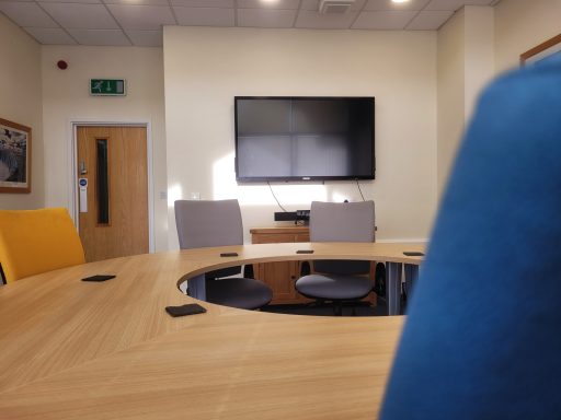 A photo of across the round boardroom table looking at the 64" TV on the wall.