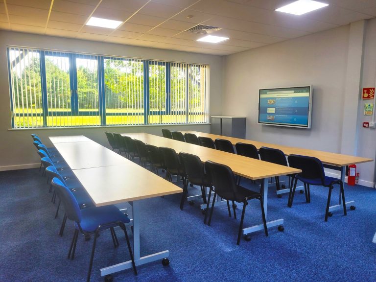 A photo of a meeting room laid out with the classroom layout with three rows of tables and chairs