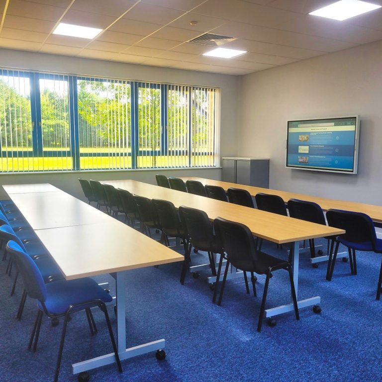 A photo of a classroom style training room with smart TV displaying a website on the wall and a view of the golf course out the window.